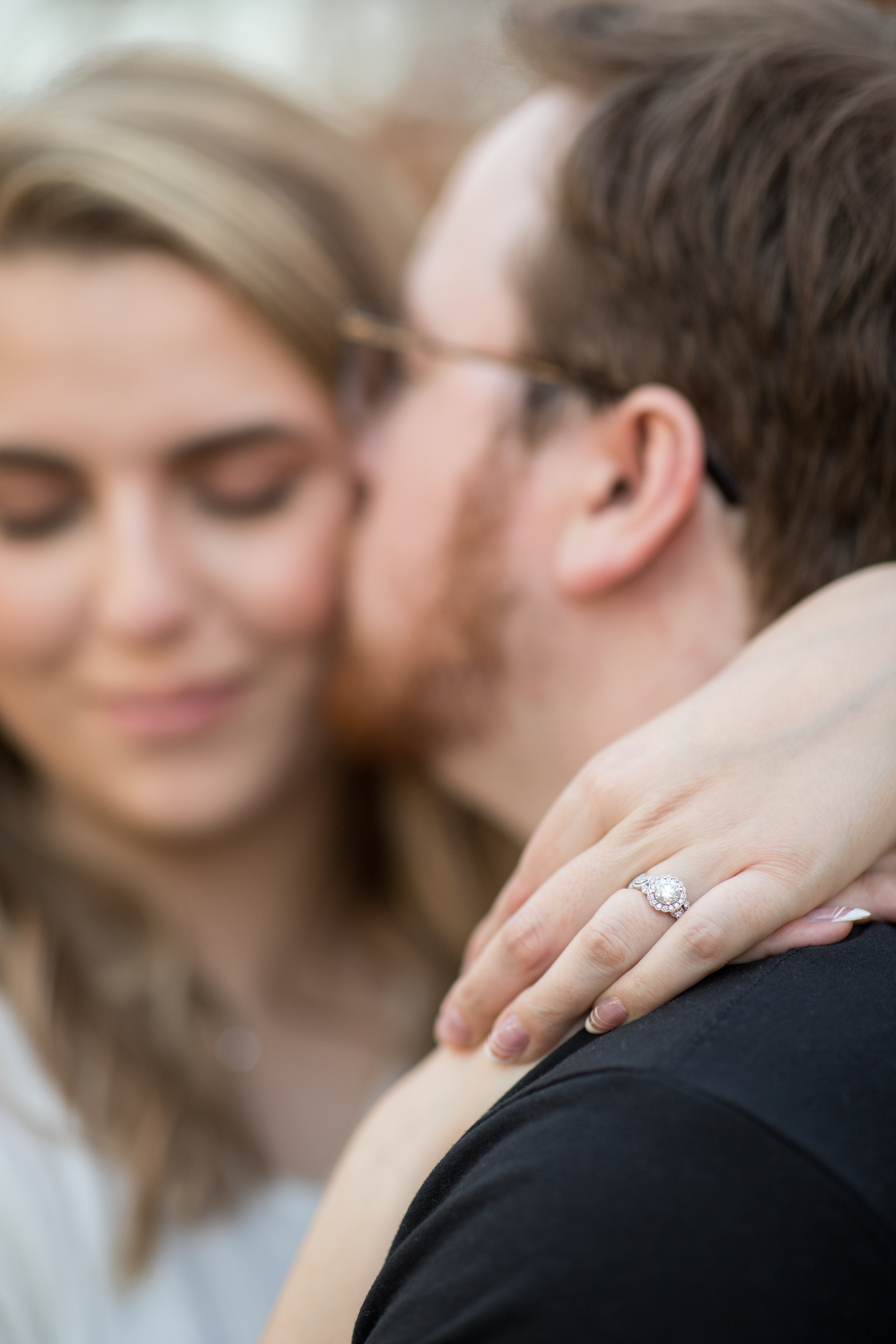 woman showing off engagement ring while fiance kisses her cheek