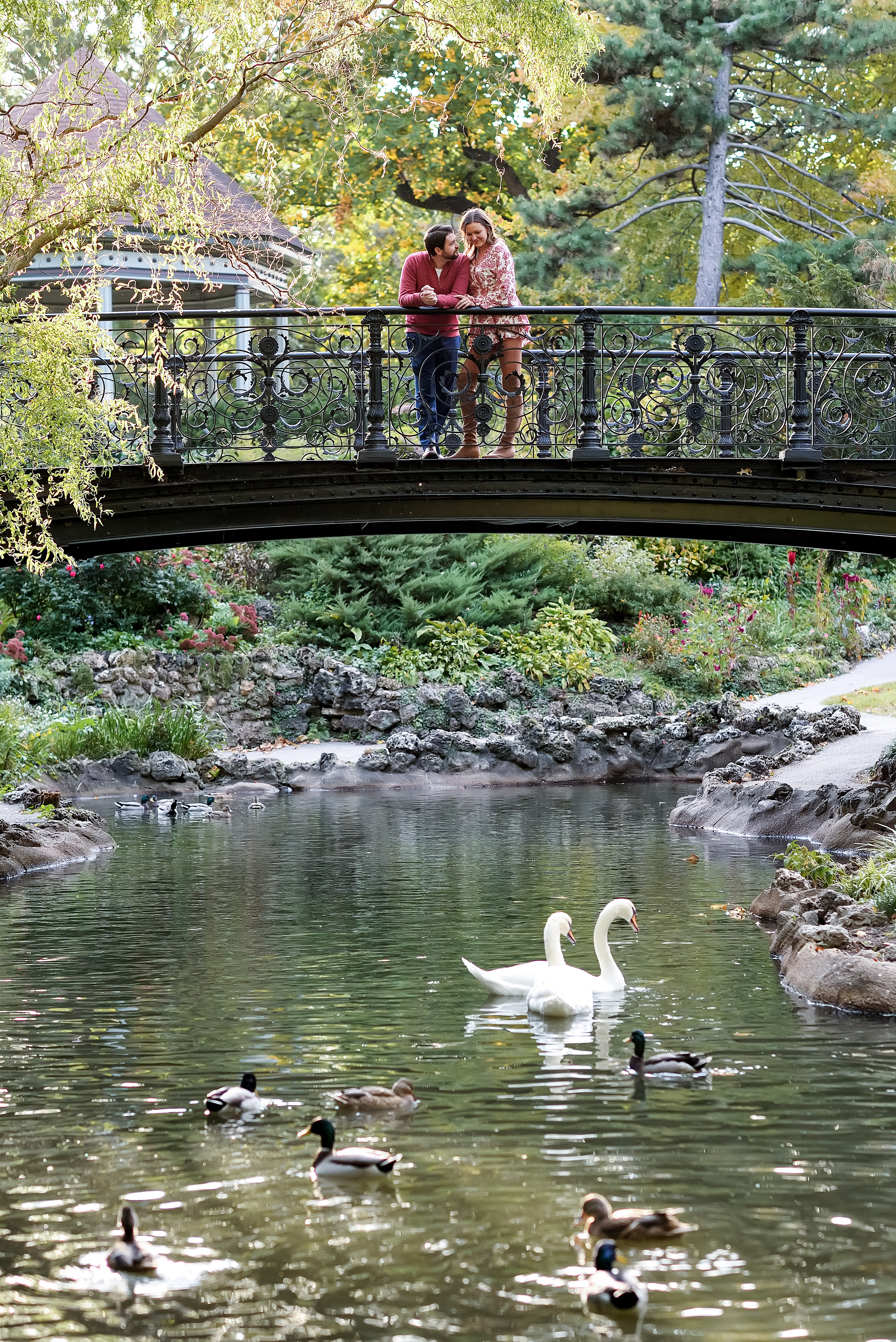 couple standing on bridge while ducks swim by