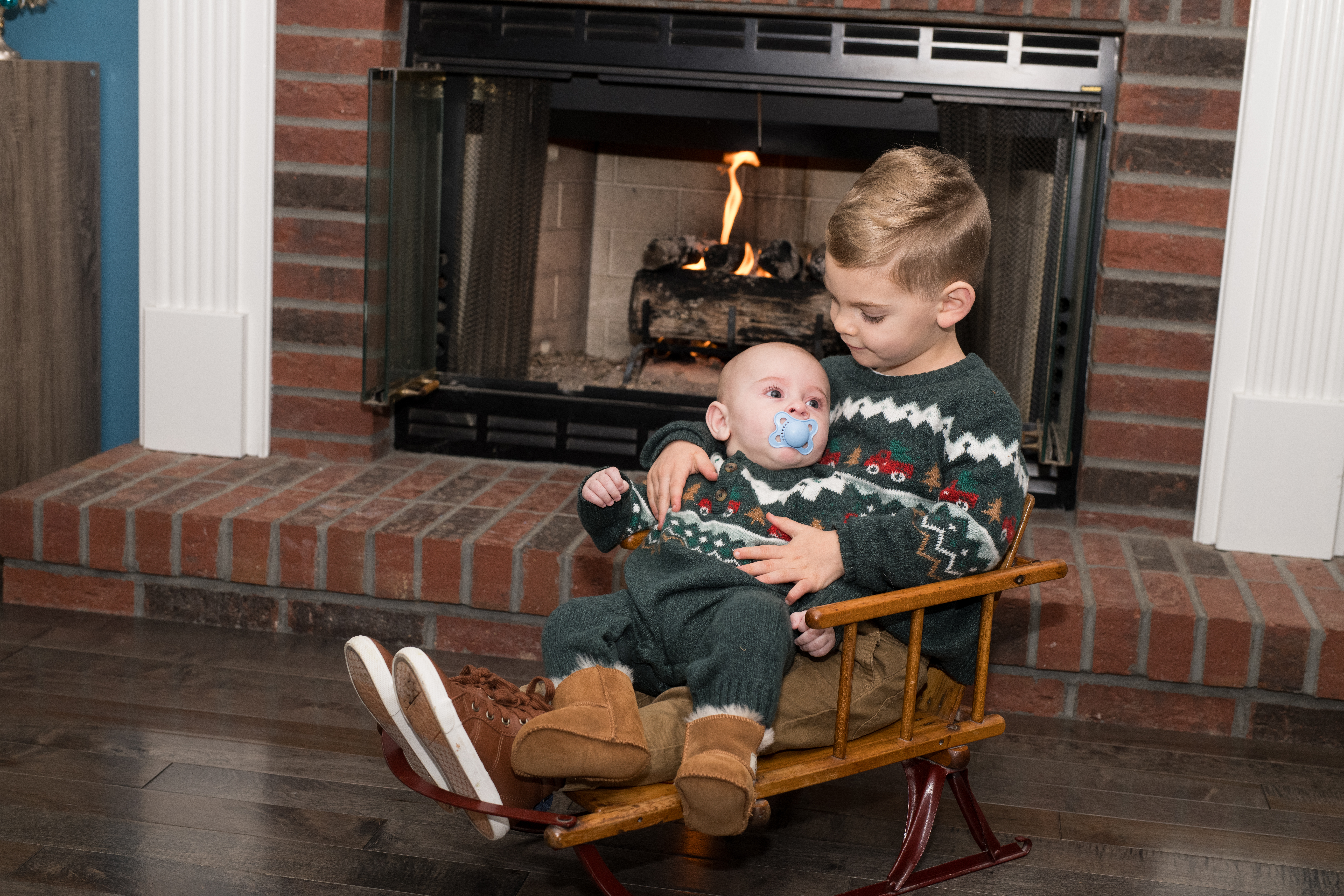 two young brothers sitting by fireplace in mini sleigh Christmas photo